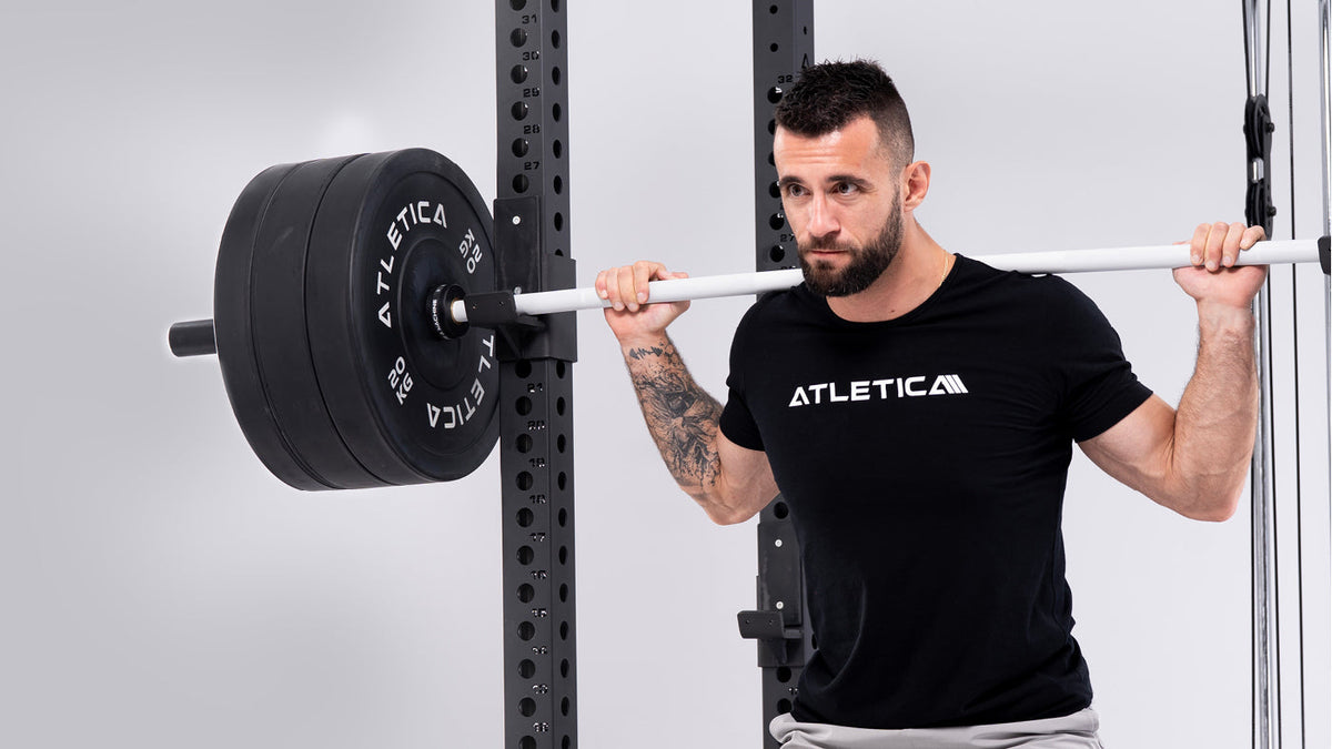 Back squat on the R8 Blackhawk Power Rack with a white barbell and black Bumper Plates