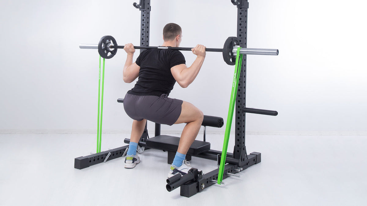 Man doing banded barbell back squats in a power rack with green Atletica resistance bands