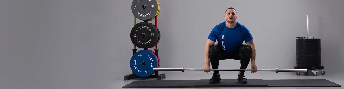 Karlos Nasar doing deadlift with the Atletica Alpha barbell - weight plates on storage next to him
