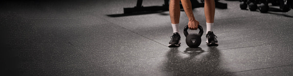 Person lifting an 18 kg Atletica kettlebell off a rubber gym flooring