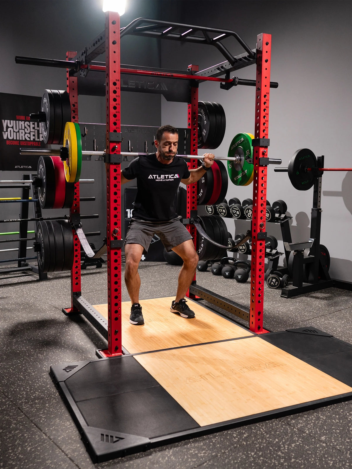 Man doing barbell back squats on the Atletica deadlift platform in a red power rack