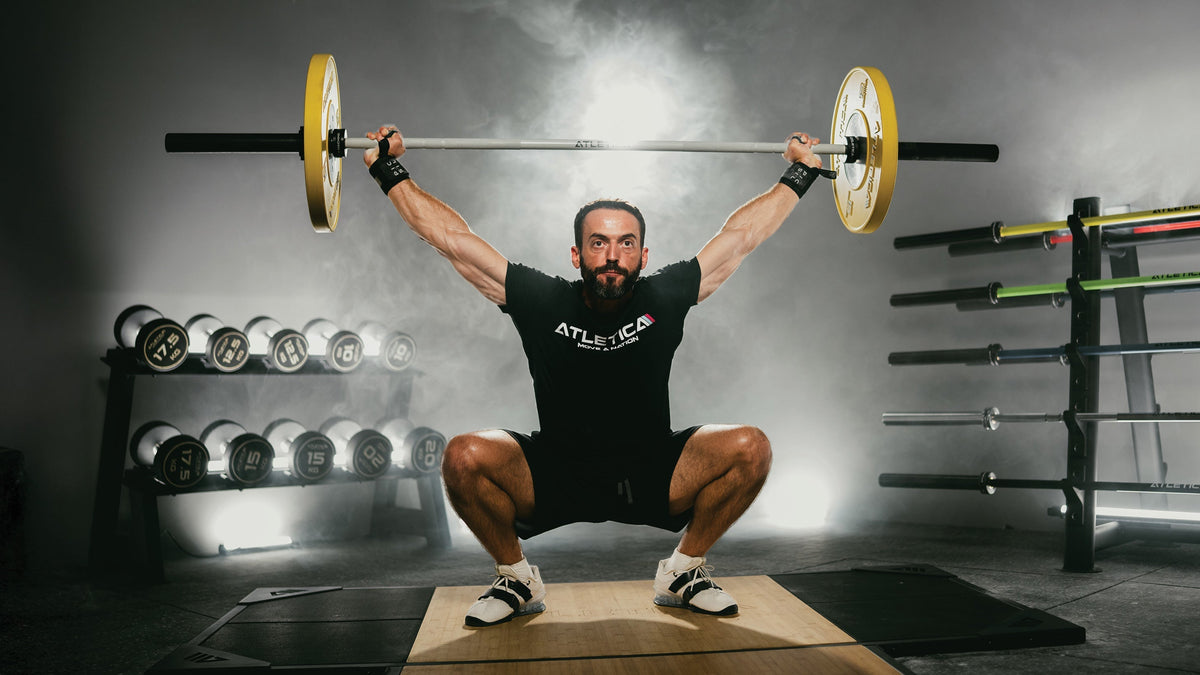 Athlete performing an overhead squat with an Atletica barbell and Color Bumper Plates in the gym