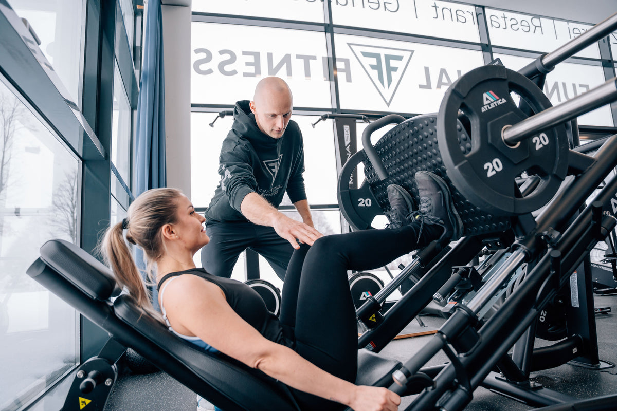 Frau trainiert an der Hyperleg Beinpresse von Atletica mit ihrem Personal Trainer im Fitnessstudio