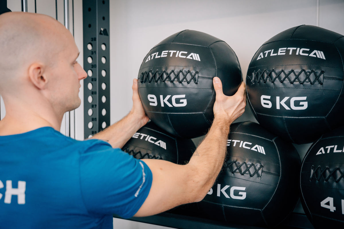 Trainer greift nach einem Atletica 9 kg Wall Ball im Fitnessstudio