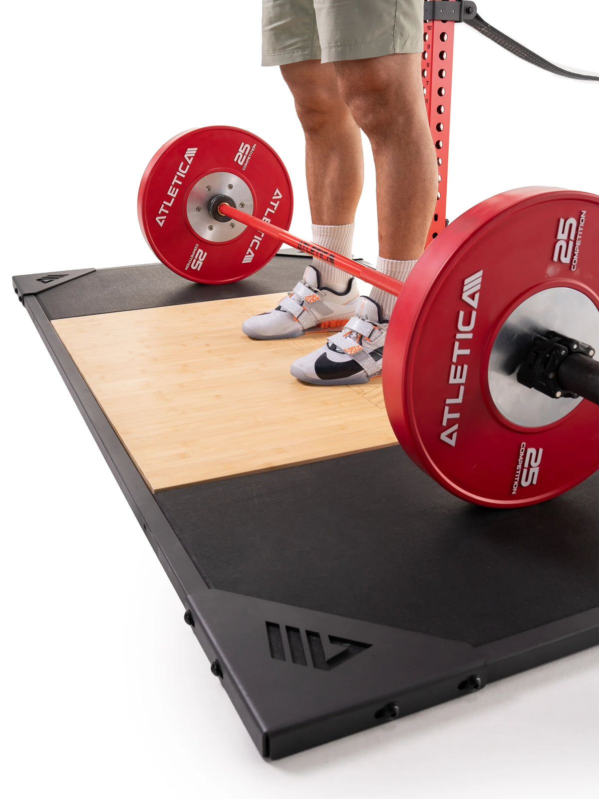 Man deadlifting a barbell with red bumper plates on the Atletica deadlift platform