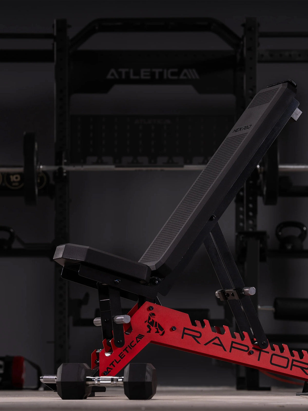 Atletica Raptor HexPad weight bench in sports car red in front of a power rack in a dark gym