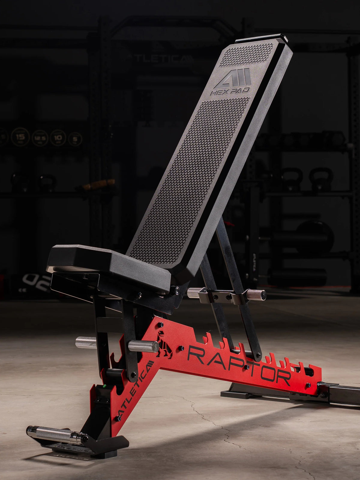 Atletica Raptor adjustable weight bench with red frame in incline position in a dark home gym