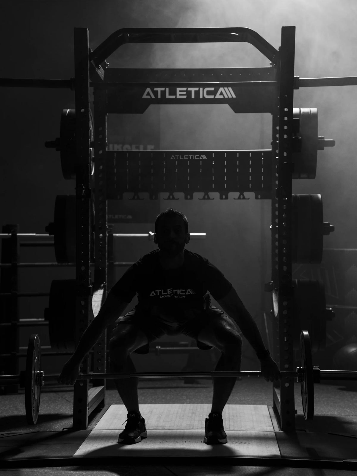 Man squatting on the Atletica deadlift platform in a power rack, black and white photo