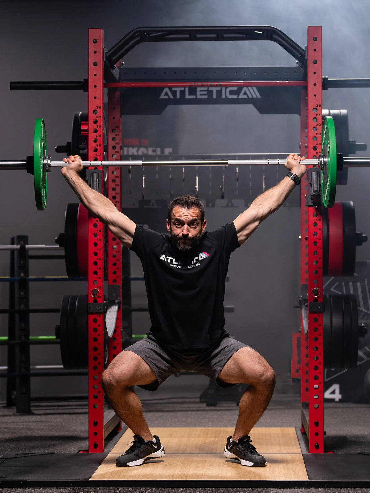 Man doing overhead squats on the Atletica deadlift platform in a red power rack