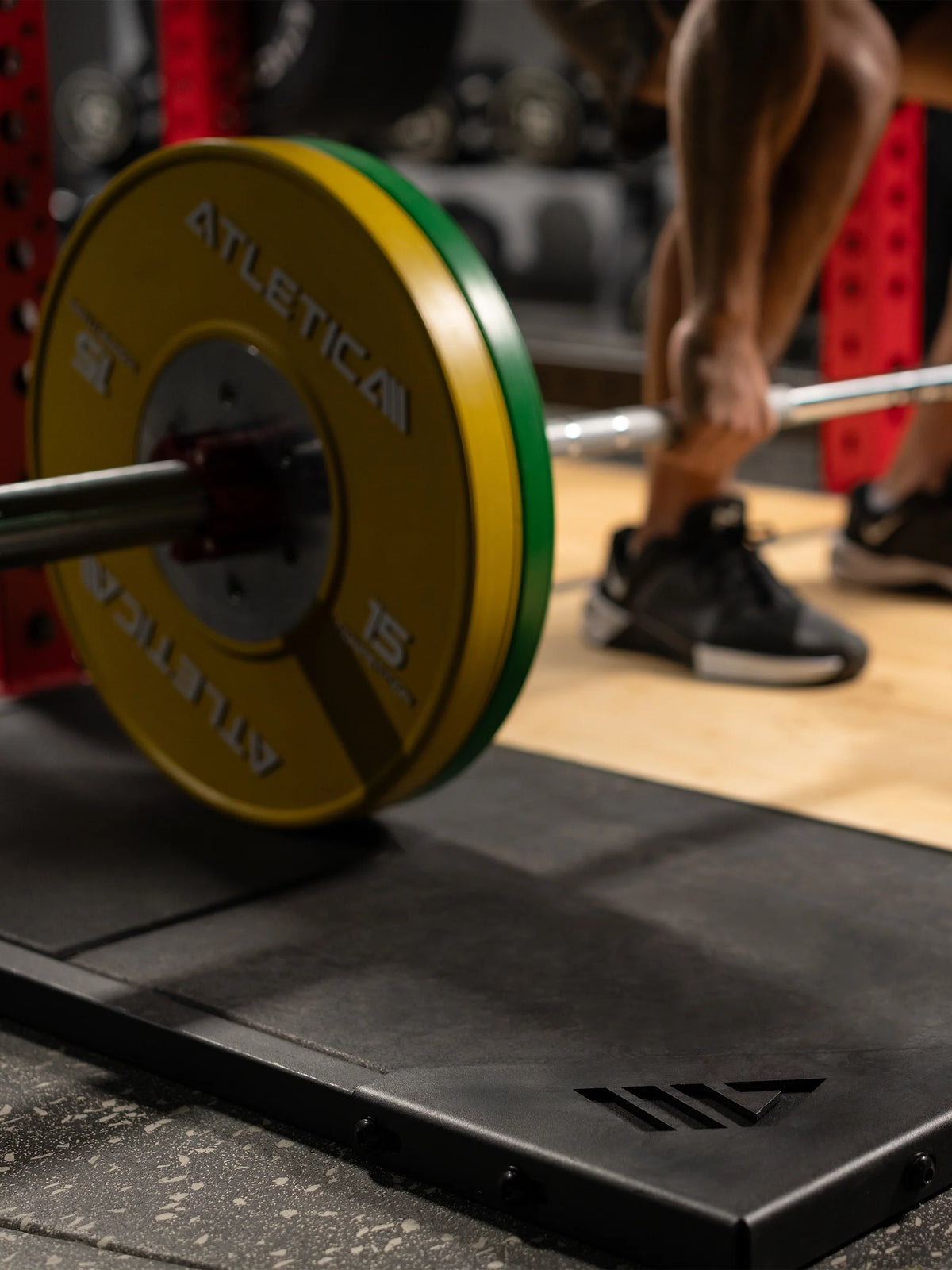 Barbell with yellow bumper plates on the Atletica deadlift platform, close-up of the rubber edge