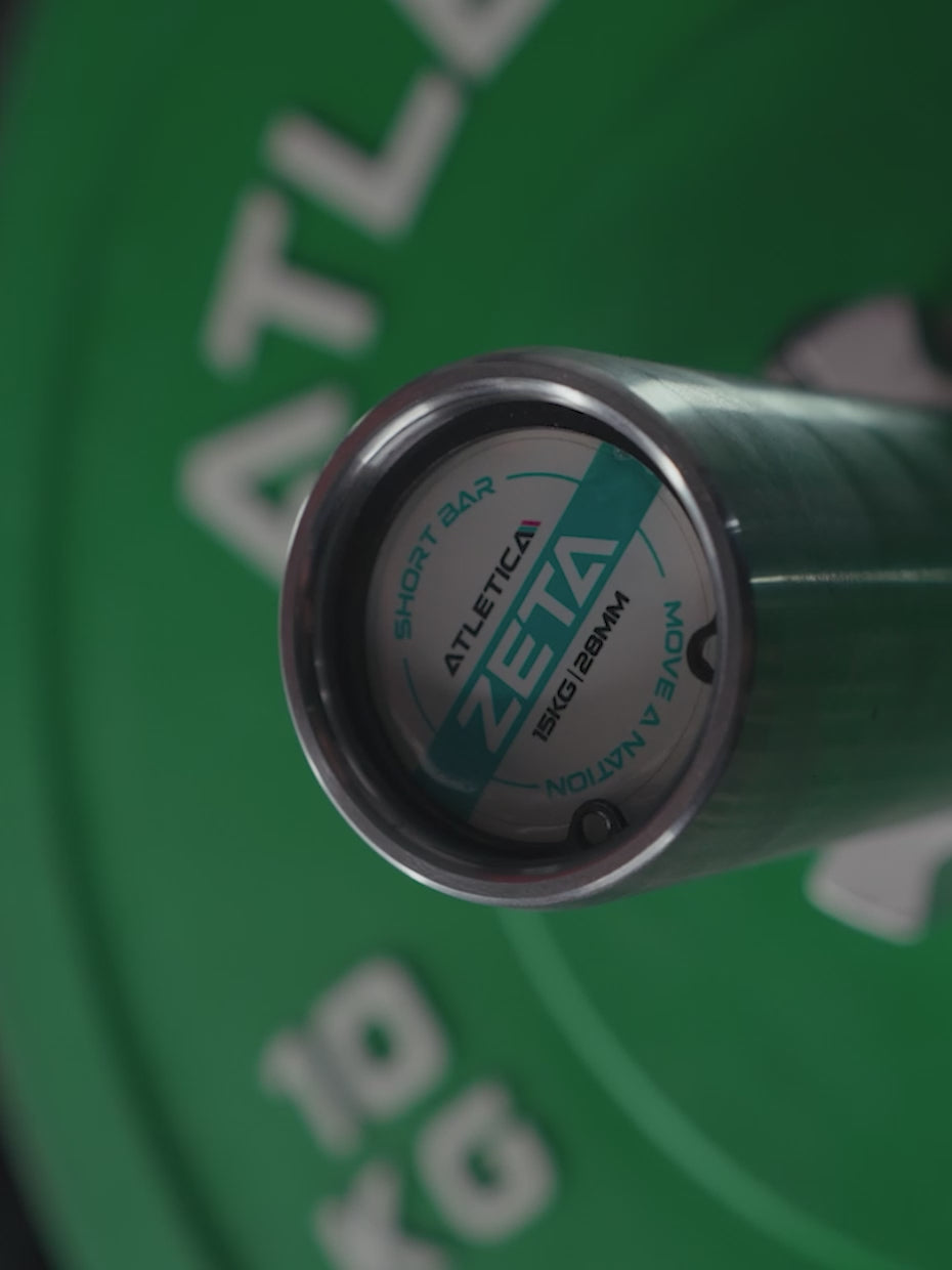 Video: Atletica Zeta short barbell, close-up of the end cap with green bumper plate behind